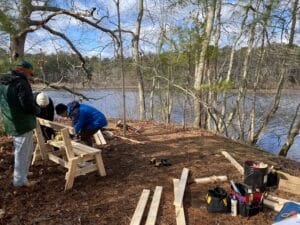 A group of people building a bench by a lake.