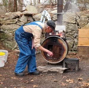 A person tending to a wood-fired stove near a stone wall.