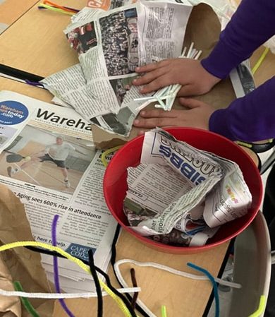 Hands crafting with newspapers and pipe cleaners